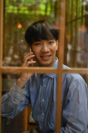Taken through the window shot of Young Businessman call with a phone while sitting in the restaurant during free time.の写真素材
