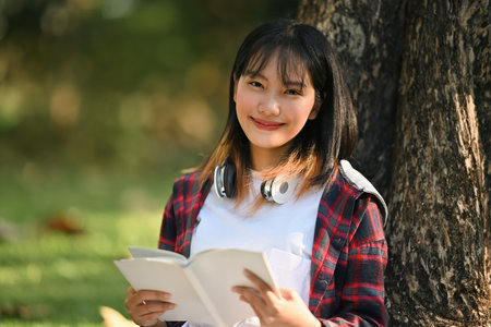 A Happy Teenage student girl reading a book while sitting at campus in spring time.の写真素材