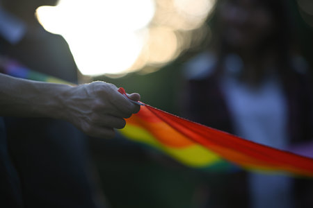 Backlit and close-up photos of a group of teenagers campaigning for gender equality and equal marriage. Focus on a hand holding rainbow flag.の写真素材