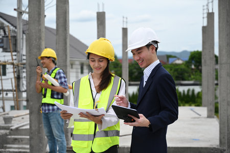 Engineer or Architect and construction workers review plans on-site, smiling and discussing project...