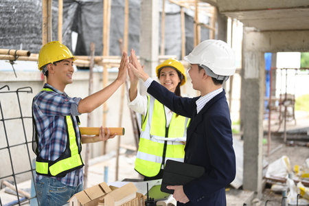 Engineers and a manager celebrating with a high-five on a construction site, reflecting teamwork and...