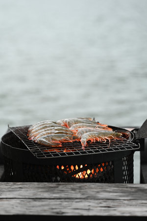 Vertical image of Raw prawns arranged on a grill over open flames, slowly cooking to perfection as the heat transforms their shells to a vibrant orange, preparing them for a delicious meal.の写真素材