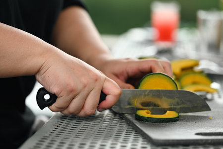 Close-up of hands slicing a Japanese pumpkin or kabocha squash on a cutting board, showcasing the...