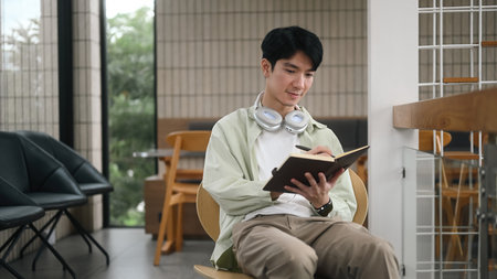 A Young adult man enjoying a quiet moment journaling in a cozy working space, surrounded by a...