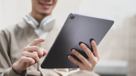 A man is sitting on a chair and holding a tablet. He is smiling and he is enjoying his time,...