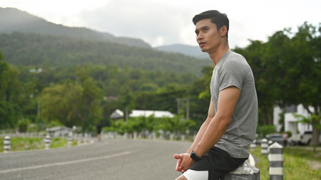 Moments of Reflection: A young man sits on a roadside barrier, taking a moment to rest after a...