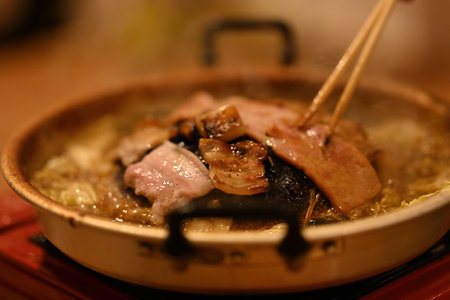 Close-up of Slices of pork cook on the hot Moo Kata grill, releasing a savory aroma as the meat sizzles and the flavorful broth below bubbles with vegetables and seasonings.の写真素材