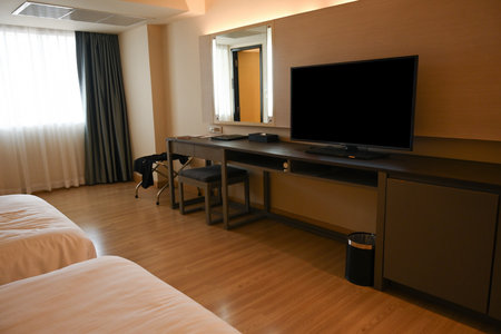 A modern hotel room features a sleek TV, and wooden desk with a mirror, chair, and soft lighting, creating a blend of relaxation and functionality.の写真素材