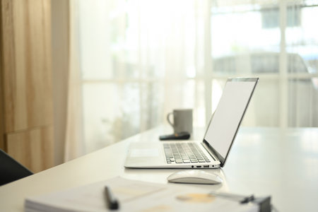 A modern workspace featuring an open laptop with blank screen, a wireless mouse, documents, a pen,...
