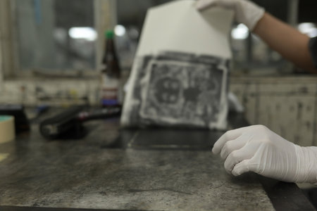 A Close-up image of a printmaker carefully lifts a freshly printed artwork from the printing plate.の写真素材