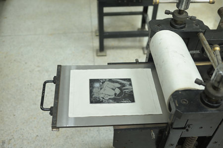 An inked artwork plate rests on the press bed of the printing press machine in a professional printmaking studio, Art of Printmaking concept.の写真素材