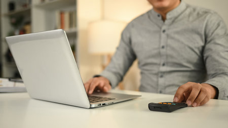 A Close-up of a businessman works on his laptop while using a calculator, focusing on financial...
