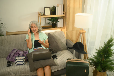 Cheerful senior woman using her phone to contact hotel or tour operator, arranging her vacation...