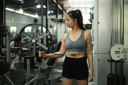 A Young Asian Woman Training with Cable Machine at Gym.