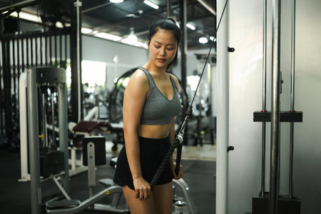 Young woman focused on triceps pushdown exercise using cable machine at the gym, building upper arm...