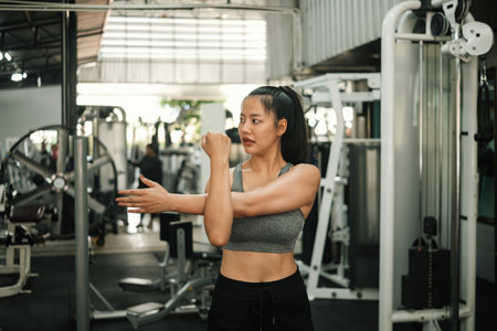 Confident young woman stretching her arm muscles at the gym, preparing for a workout.の写真素材