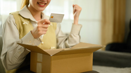 Close-up of a woman smiling, holding a credit card and raising a fist in excitement while opening a...