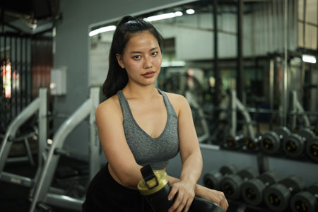 Young athletic woman confidently resting at the gym, holding a protein shaker.の写真素材