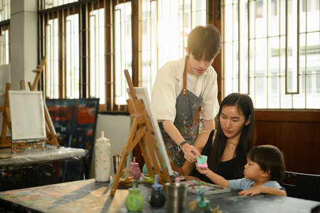 An art teacher helps a mother and her young child during a fun, interactive painting activity in a...