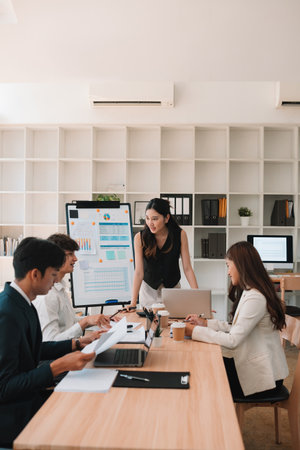 A team of young professionals engages in a strategy meeting in a bright office. A woman stands...