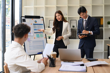 Confident businesswoman presenting charts on a whiteboard to colleagues in a modern office. Teamwork...