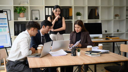 A diverse business professional team works together, analyzing documents and financial data in a...