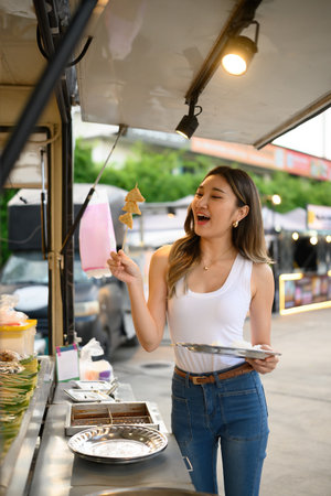 A Smiling Young Woman Enjoying Grilled Street Food Skewers, Capturing the joy of tasting local cuisine.の写真素材