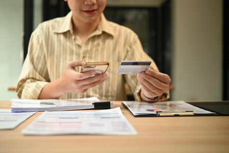 Close-up image of a young businessman using smartphone and credit card at work desk, Mobile Payment...