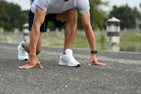 Close-up of a male athlete in starting position for a sprint, hands on the ground, ready to run on...