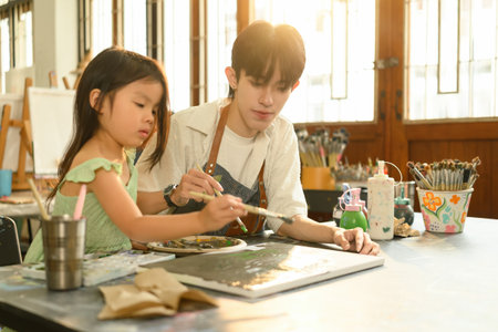 Caring teacher helps a young student explore creativity through hands-on painting activity.の写真素材