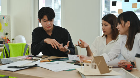 Professional design team having a focused discussion on construction plans and design solutions,...