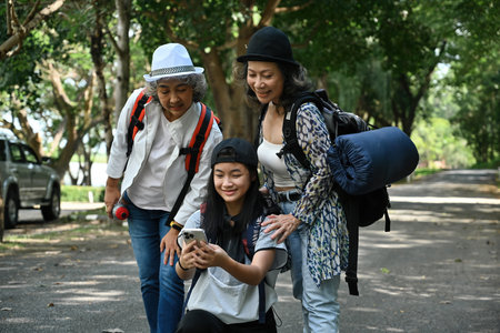Granddaughter shows two grandmothers the route on a smartphone while hiking. A joyful...