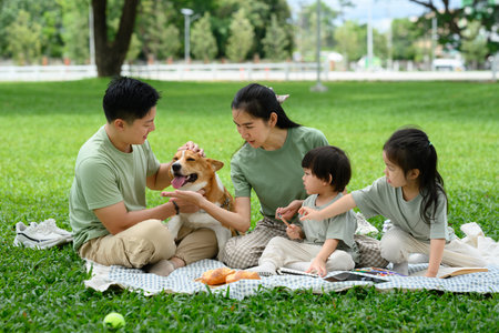 A joyful family shares laughter, snacks, and dog cuddles on a sunny green law.の写真素材