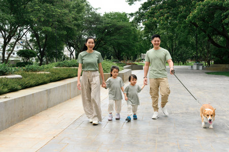 An Asian Family of four enjoys a relaxing walk through a city park with their cheerful Corgi, holding hands and smiling.の写真素材