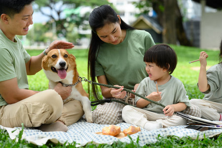 A young boy shows surprise at a dog while his parents take care of him, a family picnic in a park.の写真素材