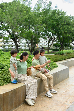 A Parents and children relax with their corgi in a peaceful green park, showcasing warmth, connection, and pet love.の写真素材