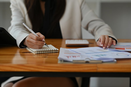 Cropped view womanâs hand writing a not and using a calculator in the office, working on data, charts and documents on the table, for finance and technology concept.の写真素材