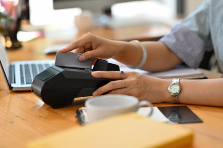 Cropped view of a woman sitting in the office swiping a credit card with a credit card swipe...