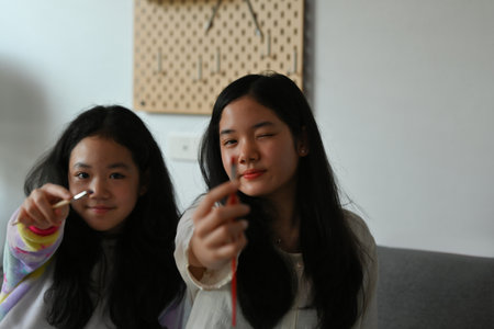 A portrait of smiley Asian girls holding a paint brush and holding out to the camera, for art,...