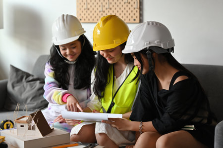 A portrait of three pretty Asian girls wearing a helmet, playing roles as architecture or engineering and looking at the paper together, for education, career and safety concept.の写真素材