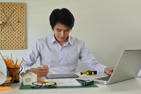 A portrait of an architecture working on a blueprint with tools and machine on the table in the...