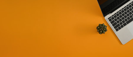 The top position view of a laptop computer next to a cactus with orange as the background ready for...