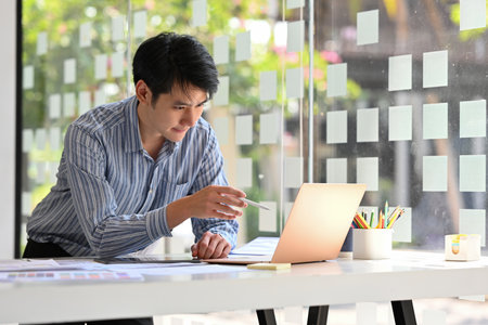 Handsome Asian Businessman in casual blue shirt use stylus pen point at the laptop.の写真素材