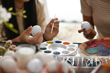 Close up with Asian sister painting Easter egg with water acrylic color on table over blurred Easter holiday decoration.の写真素材