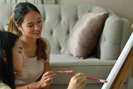Artist painting easel in home studio. Art teacher and kids girl paints with palette watercolor paints palette. Courses on drawing for children and adults.の写真素材