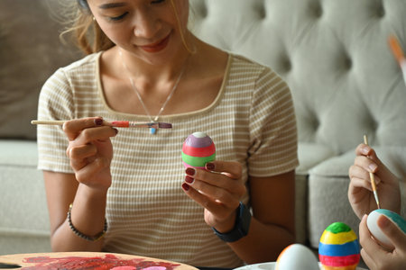 Portrait of Asian pretty female smailing while painting colorful Easter egg next to her sister. Getting ready for holiday.の写真素材