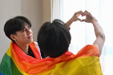 Two gay men couple doing heart shape with hands and cover with LGBT flag.の写真素材