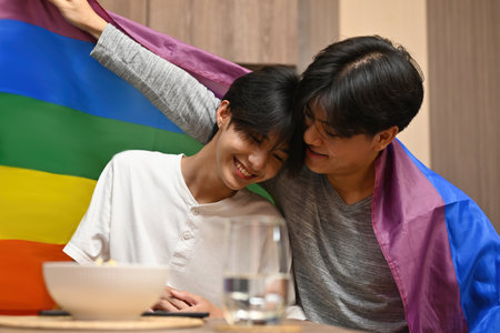 Asian gay couple having happy moment and embracing with LGBT flag, LGBT couple lifestyle, Pride month, relationships and equality concept.の写真素材