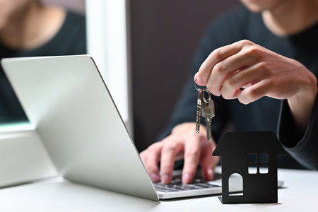 Close up of house's model over blurred Asian businessman holding a key ring and using a computer...