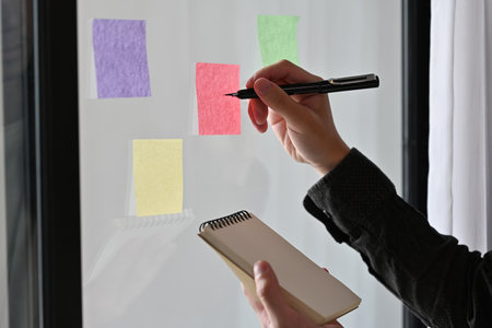 Cropped view portrait of a man taking note on a sticky note while holding a note pad. For business...